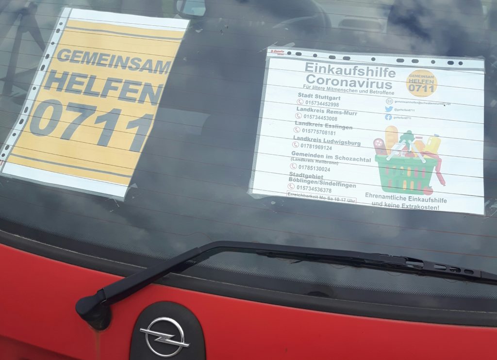 Das Bild zeigt einen roten Opel Corsa auf dessen Heckscheibe zwei Flyer Kleben. "Gemeinsam helfen 0711" und "Einkaufshilfe Coronavirus". Während der Corona-Krise kaufen VfB-Fußball-Ultras für Senioren ein.