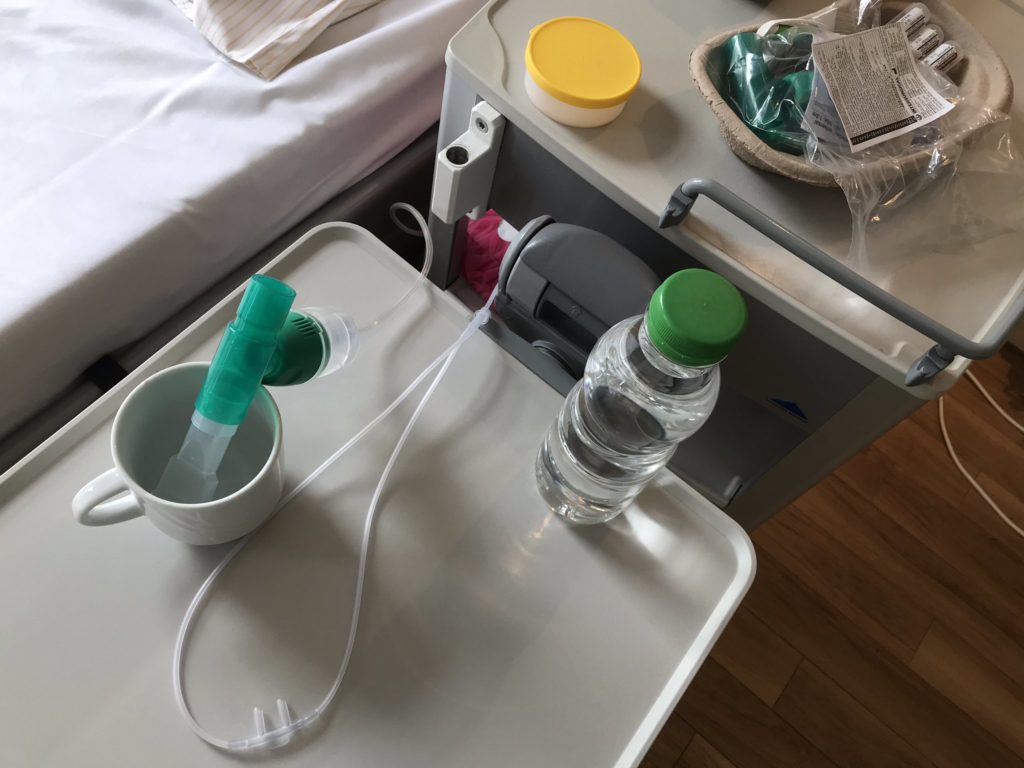 Isolationszimmer im Krankenhaus mit Bett, Wasser, Handschuhe und Asthmaspray