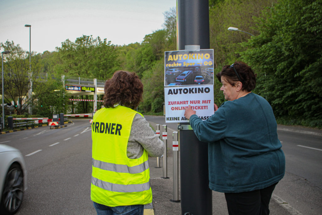 Sibylle Tejkl und eine ehrenamtliche Helferin kleben einen Flyer vor den Eingang des Autokinos. 